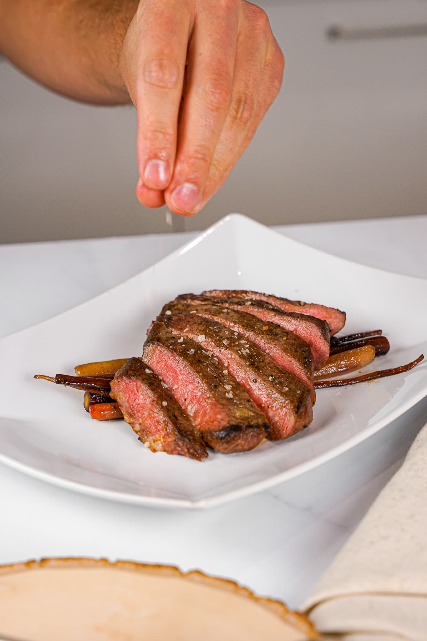 A private chef finishing a restaurant-plated dish of sliced beef with roasted carrots
