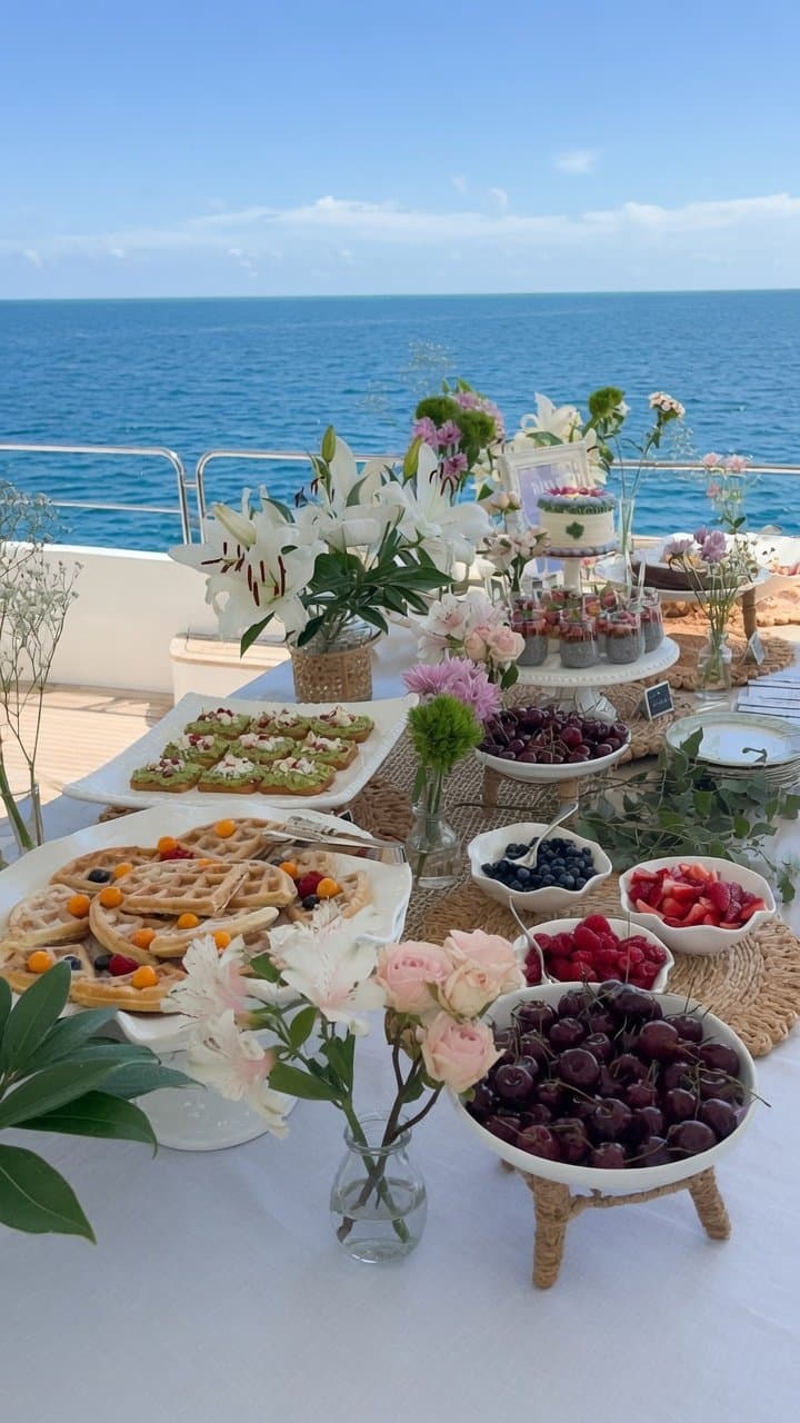 A yacht brunch spread with waffles, fresh fruit, and flowers at sea
