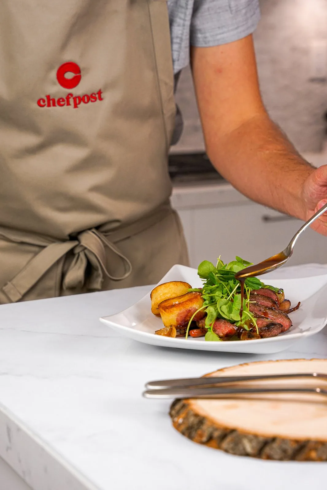 A chef in a Chefpost apron adding sauce to a plated dinner